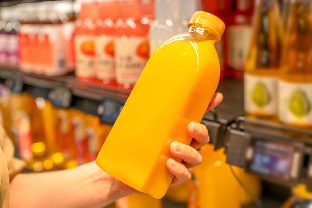 Person holding a bottle of orange juice in a supermarket