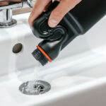 Removal of blockage in the sink, the hand of a man with a bottle of a special remedy with granules. Clean the blockages in the bathroom with chemicals.